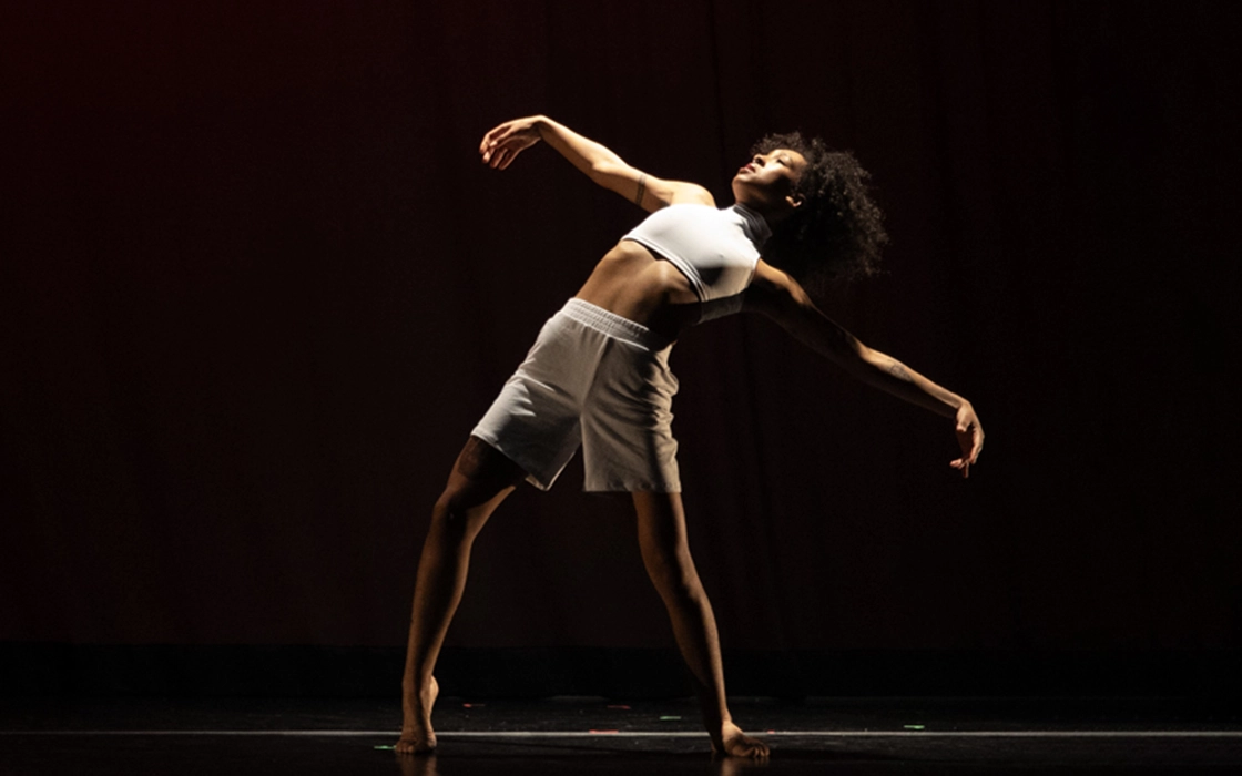 A dancer leans back with arms raised to the side in a dramatic pose.