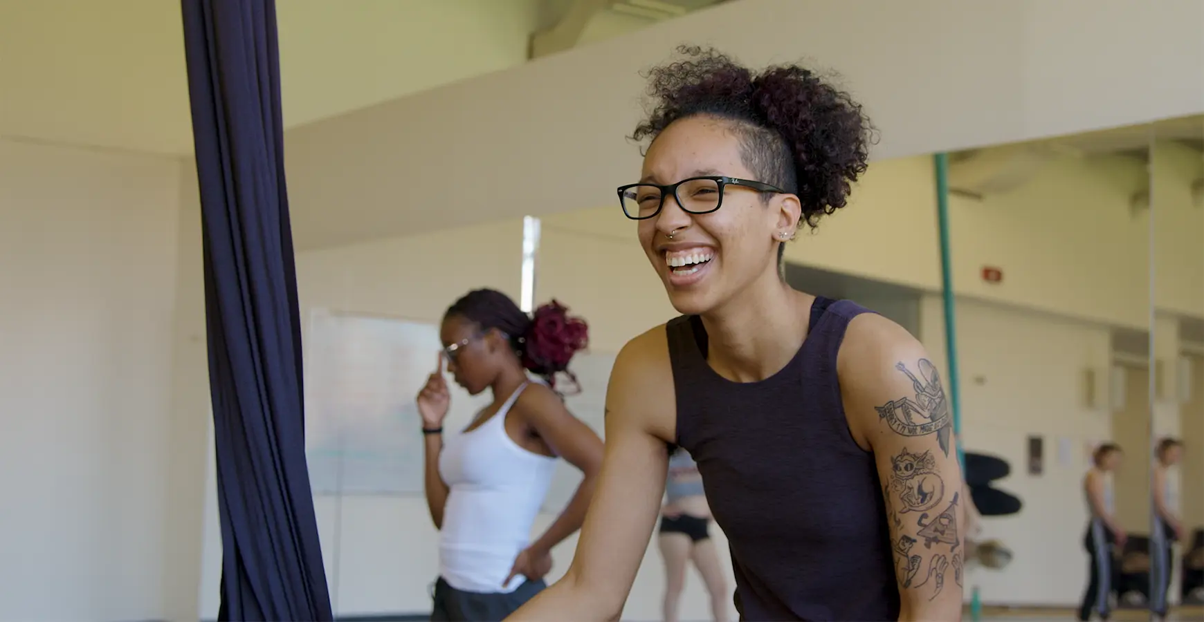 A student laughs in a dance studio. A wall of mirrors is behind her. 