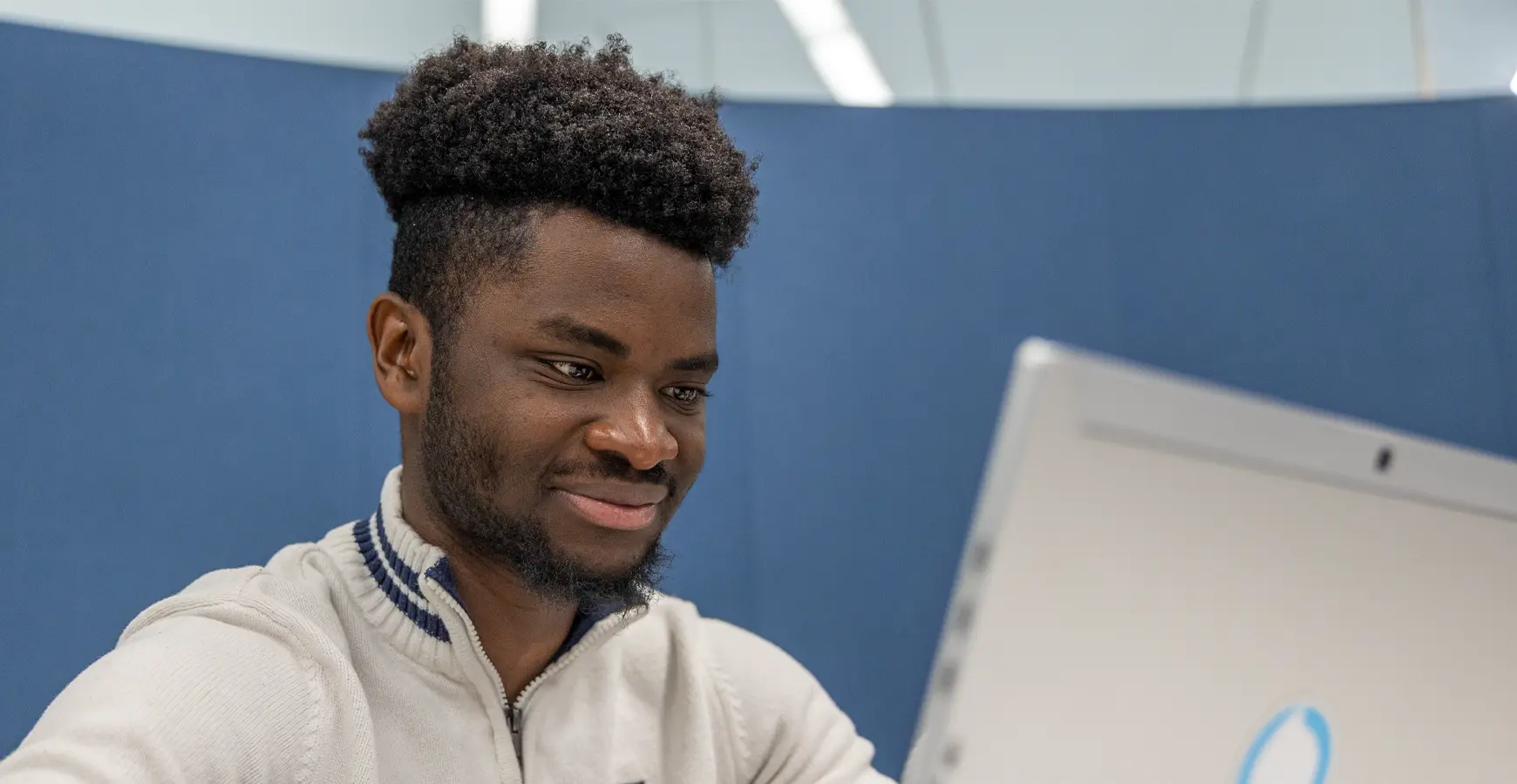 A student smiles slightly as he works on a laptop.