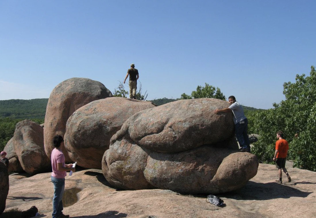 Four students climb on a giant rock formation. A forest is visible in the distance.