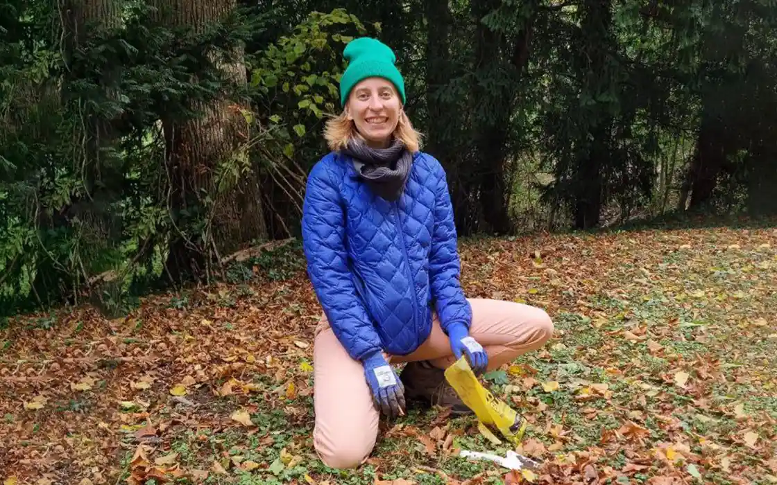 Kaitlyn Pierce kneels on the ground, which is covered in leaves. A line of trees is visible behind her.