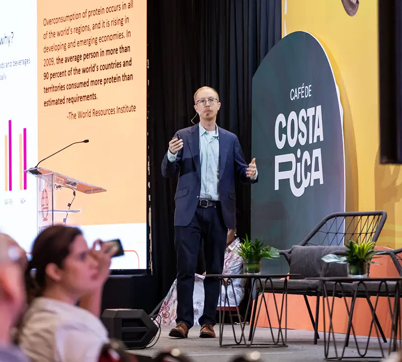 Matt Barry stands on a stage giving a presentation. A slide is projected behind him with a quote from The World Resources Institute.