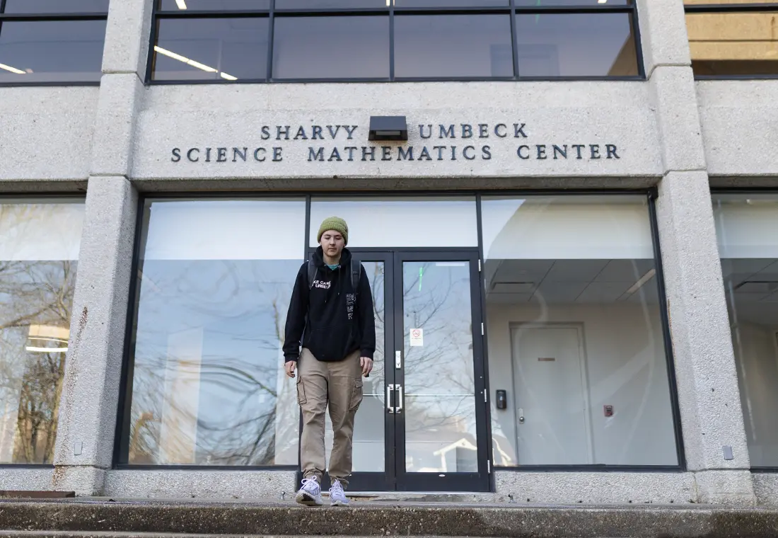 A student wears a knit cap and steps outside of the Sharvy Umbeck Science Mathematics Center.