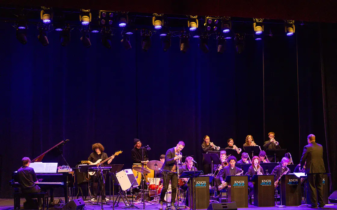 The Knox Jazz Ensemble performs on stage under lighting that casts purple hues on the musicians.