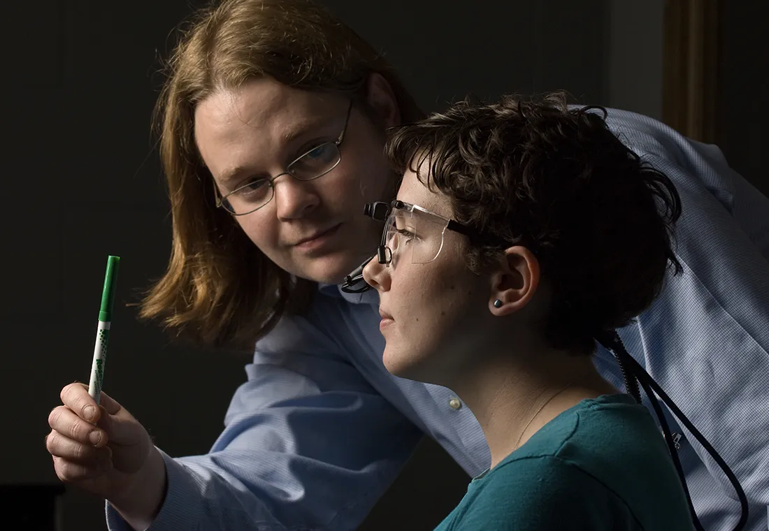 One individual holds a marker out in front of the other, performing a vision test.