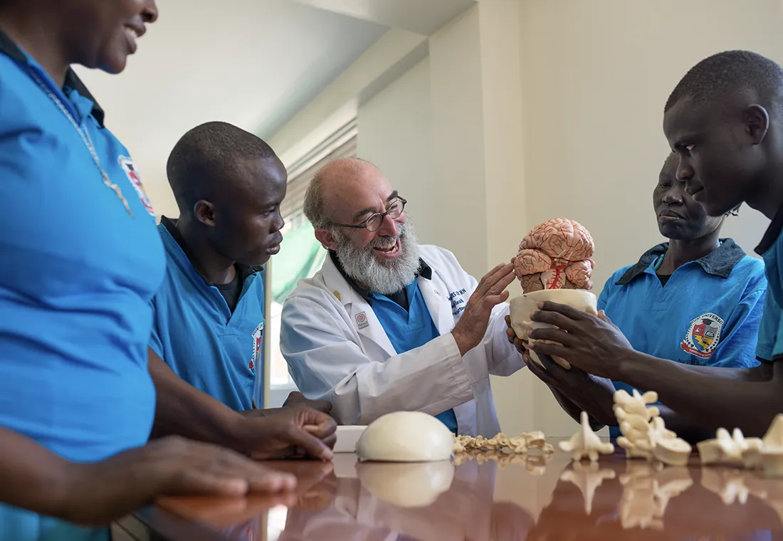 A Peace Corps volunteer wearing a lab coat teaches teaches a group of children about the human brain. 