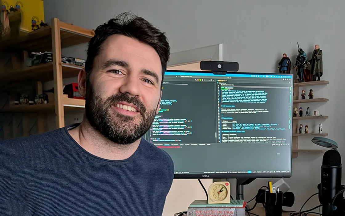 James Sheppard smiles at the camera. A computer screen is visible behind him.