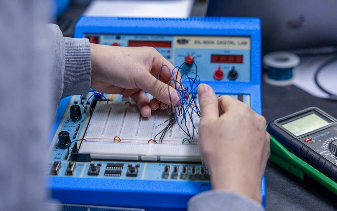  In Physics 242 class, a student works with electronics. Only the student's hands are visible.