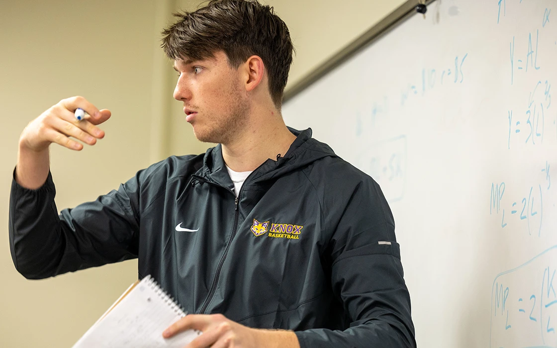 A student in ECON 301 Microeconomic Analysis class stands in front of a whiteboard and presents to the class.