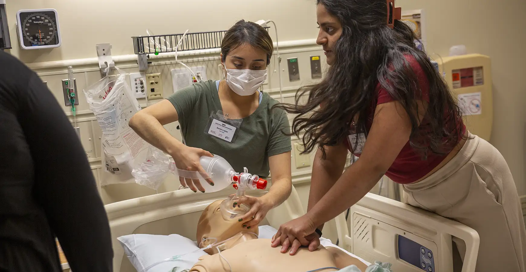 Two students work on a CPR doll in a hospital setting.