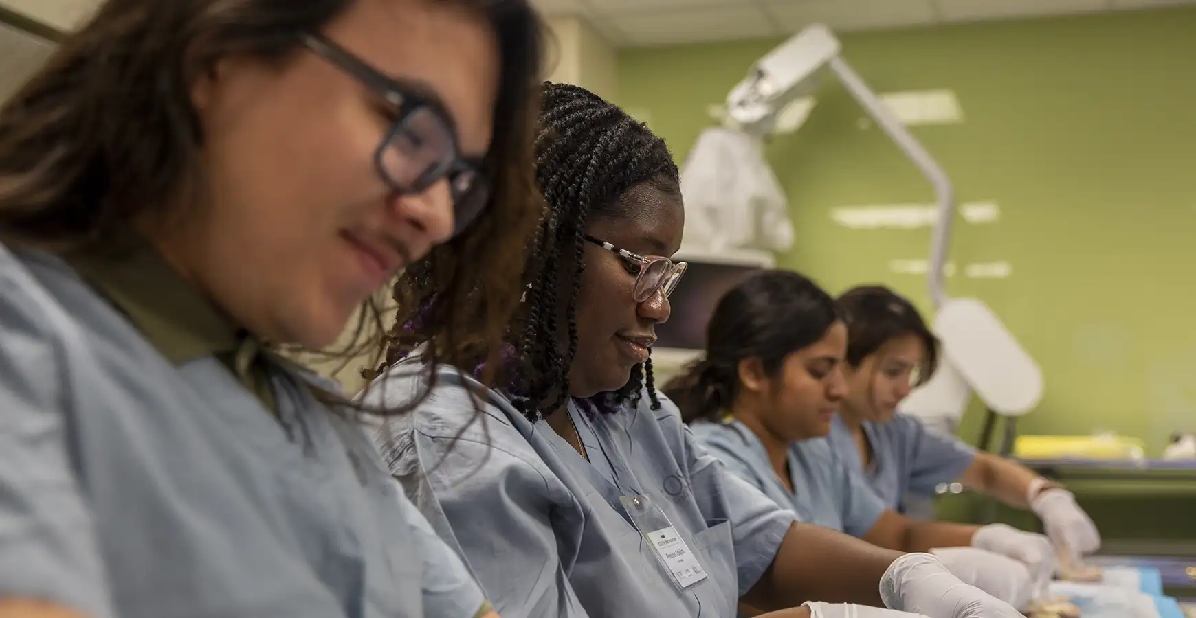 Four students sit in a line working in a suturing setting.