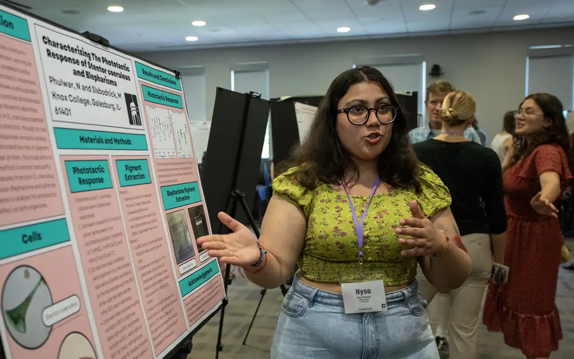 A student gives a research presentation in front of a poster.
