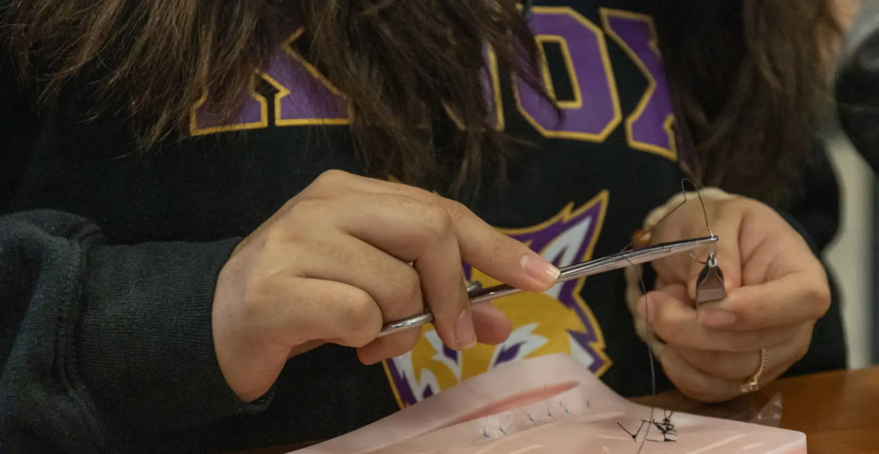 A close up of a student's hands working on the suture kit.