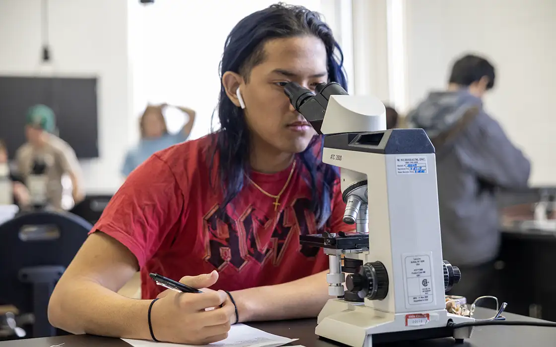 A student looks into a microscope in a classroom.