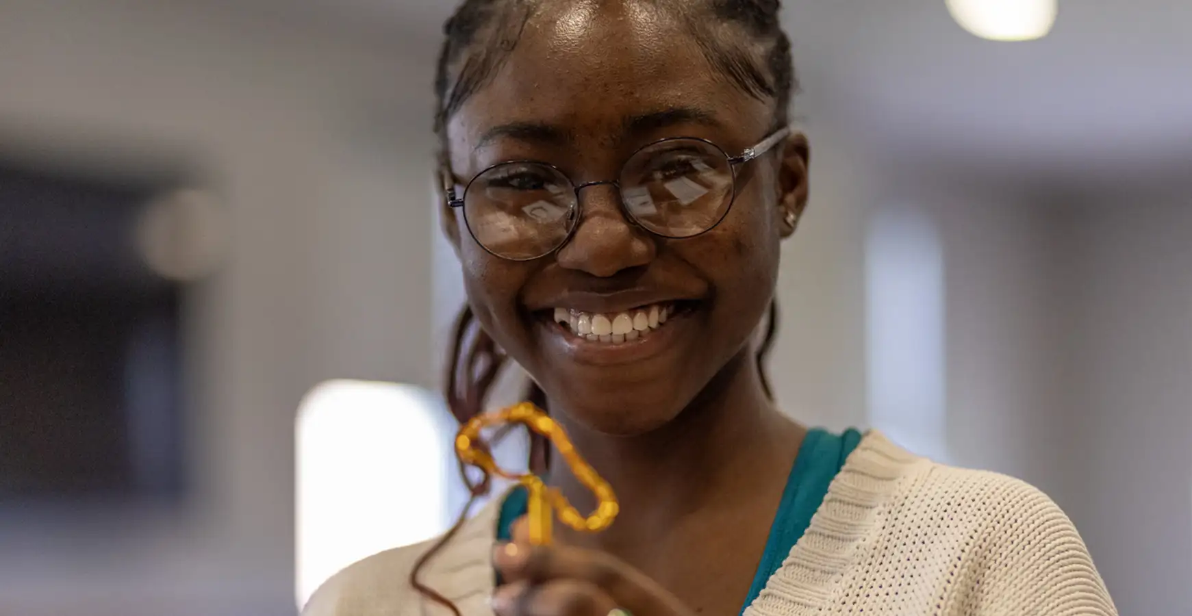 A student smiles at the camera holding a small pen shaped like a foot.