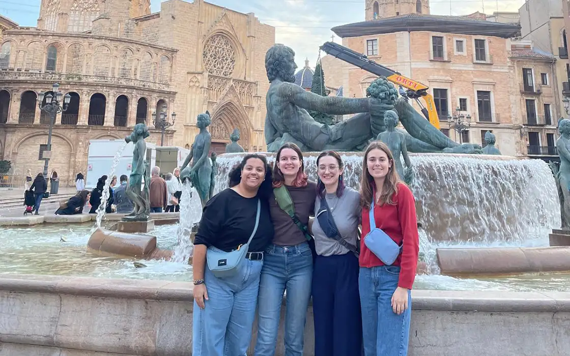 Four students stand in front of a fountain with a statue in it from a different country.