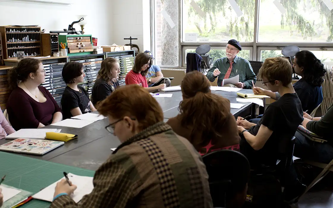 A group of students sit around a table working on their writings with an instructor.