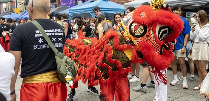 A traditional Chinese dragon puppet dances in the street, surrounded by onlookers.