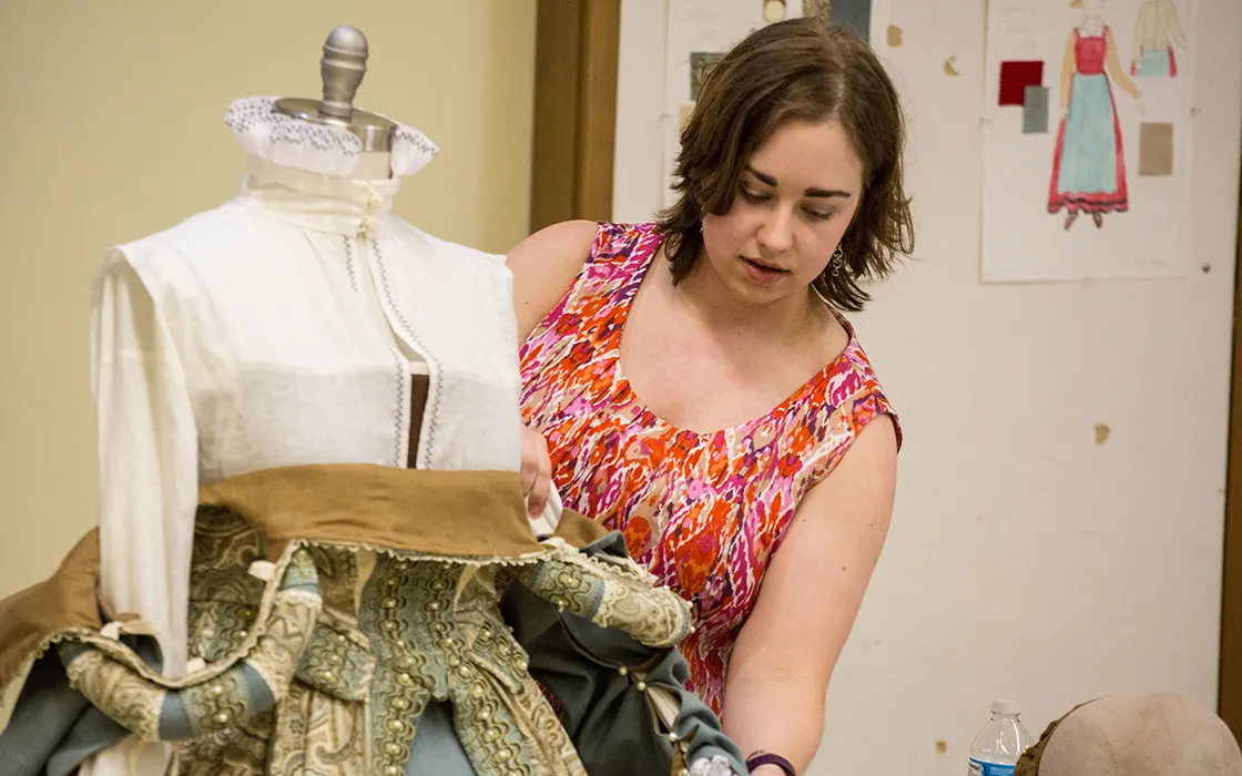 A student holds the sleeve of an ornate antique costume, looking down at it.