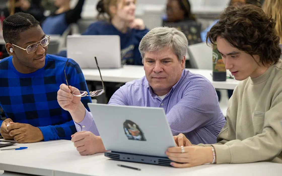 Two students look at a laptop screen with Professor Ole Forsberg.