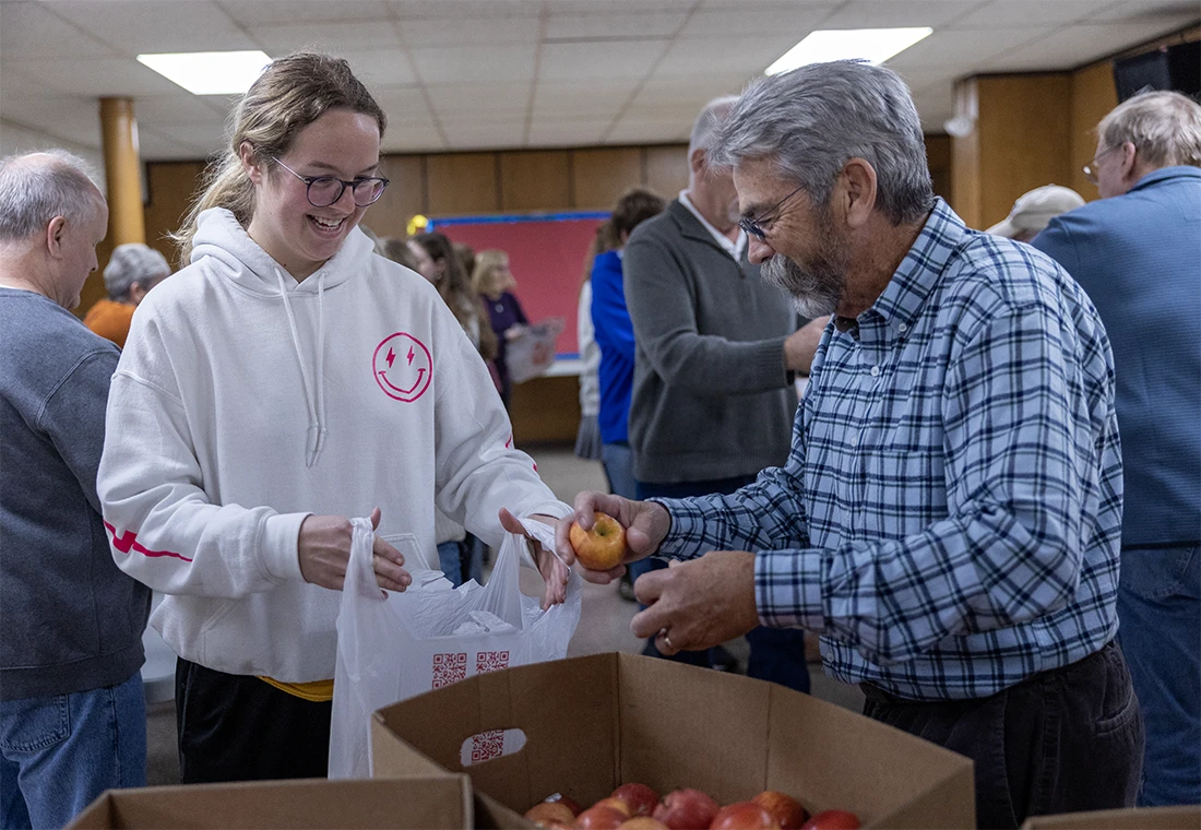 A student holding a bag while another volunteer fills it with food for Blessings in a Backpack.