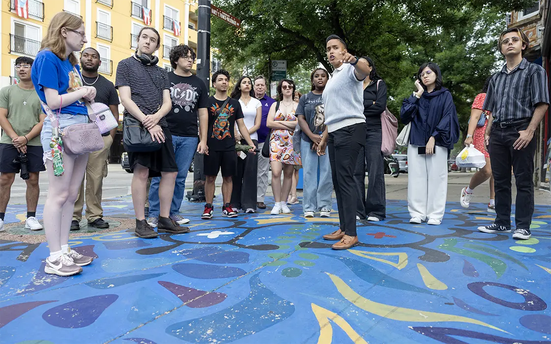 a large group of people stands around a mural painted on the ground looking at their surroundings.