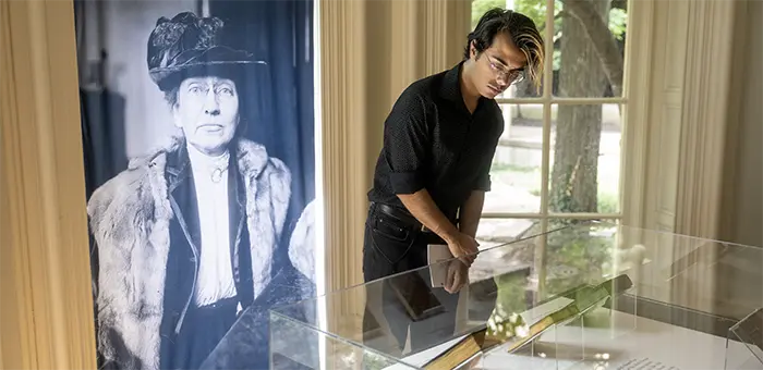 A student stands at an exhibit with a black and white photo of a woman behind him.