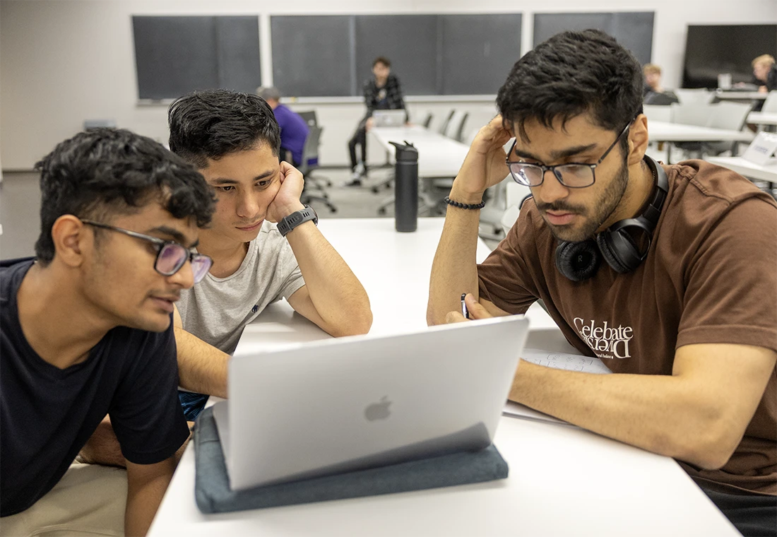 Three students look thoughtful as they study a laptop together. 