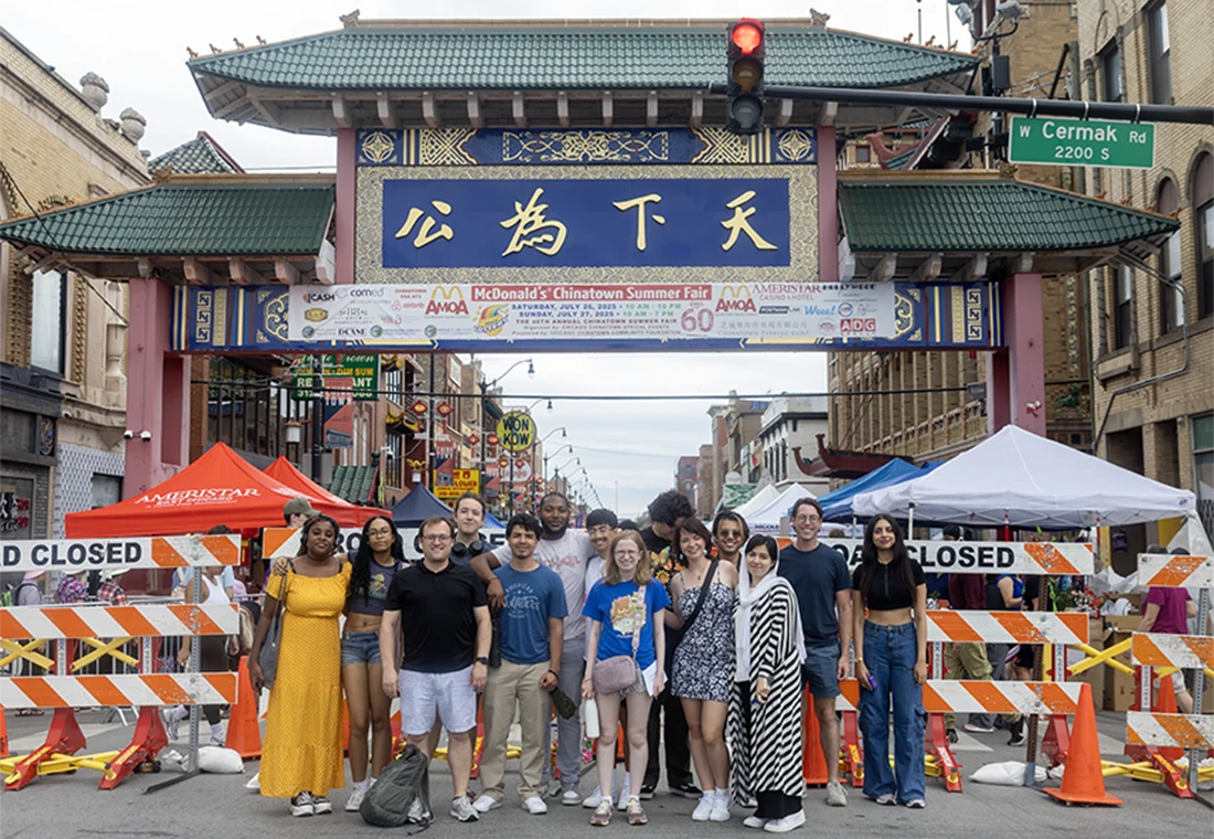 A group of students stands in front of a building that has Chinese writing on it.