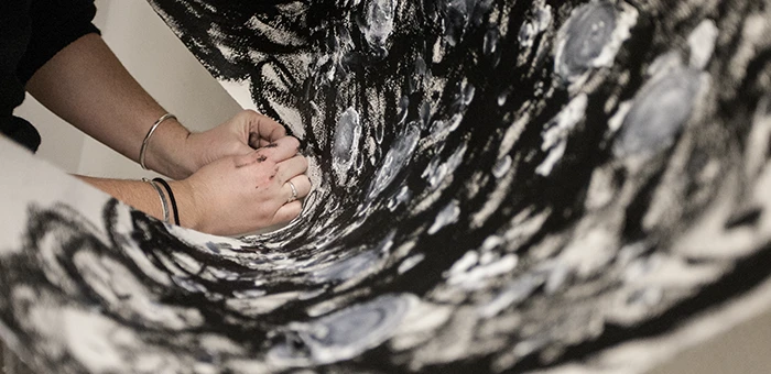 Hands unroll a black, gray and white abstract painting.
