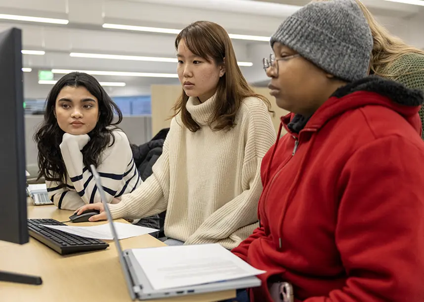 A group of students stands around a computer looking at the screen.