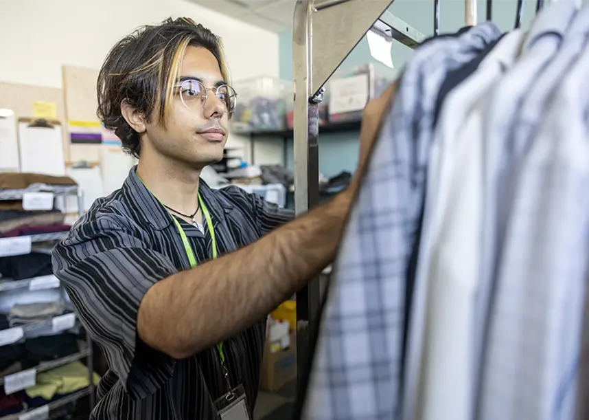 A student stands next to a rack of clothing, working on item.