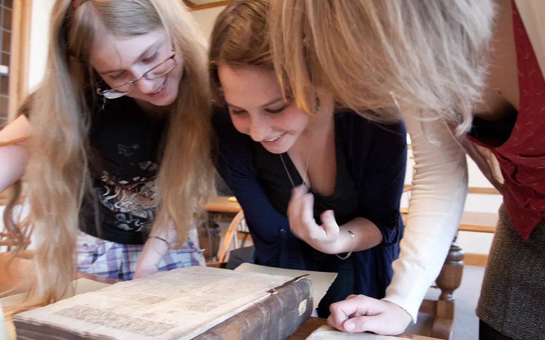 Three students lean over an archived book.