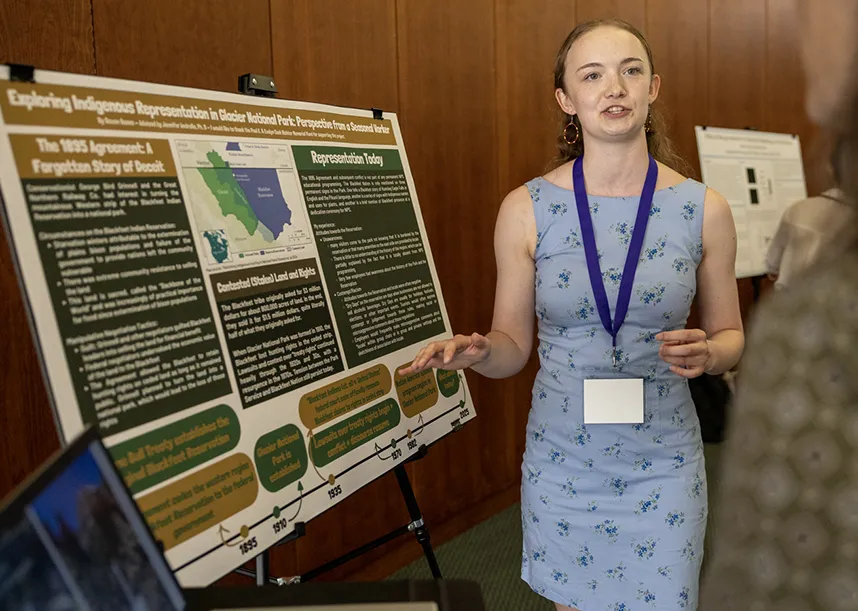 A student presents next to a poster board.