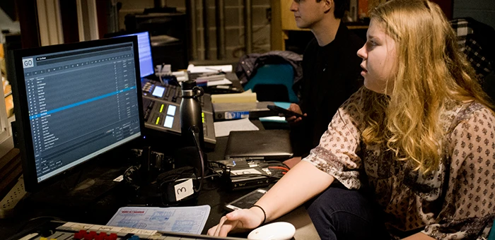 Two students sit in front of a computer in a dark room.