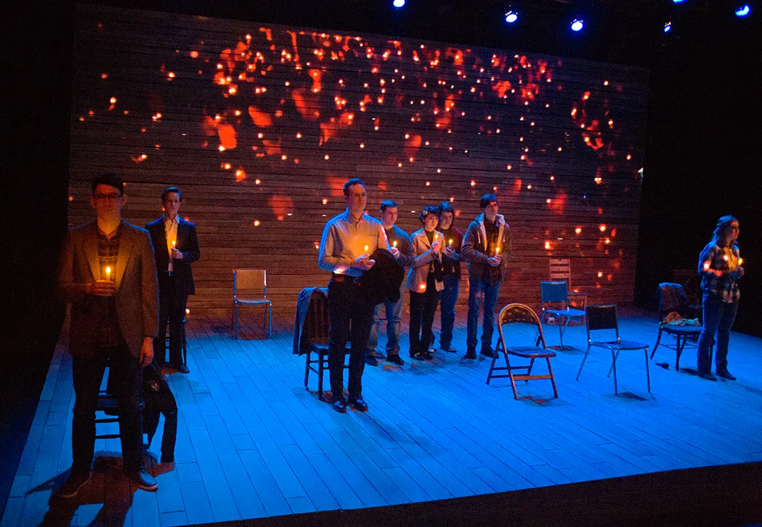 A group of people stand on a stage while holding candles.