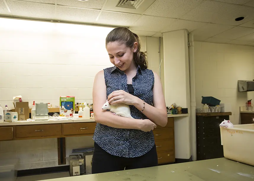 A student standing in a lab holding a white rat.