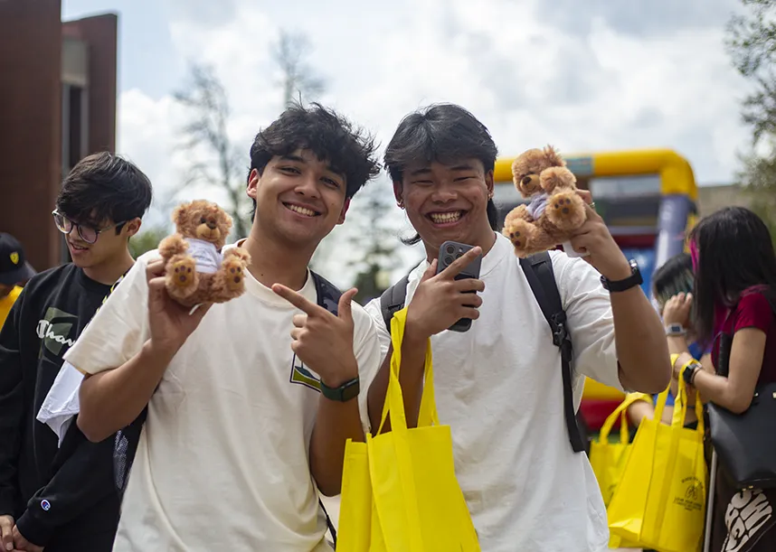 Two students hold little toy bears and smile at the camera while at an outdoor event.