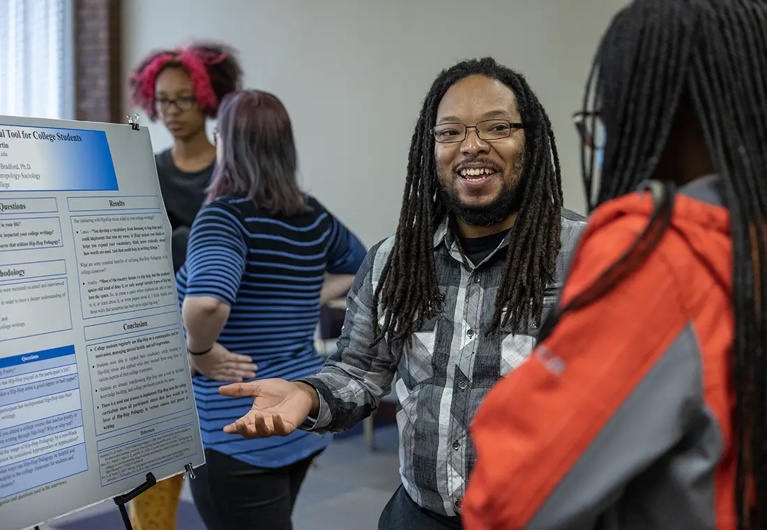 A student giving a presentation on a research project while standing in front of a poster.