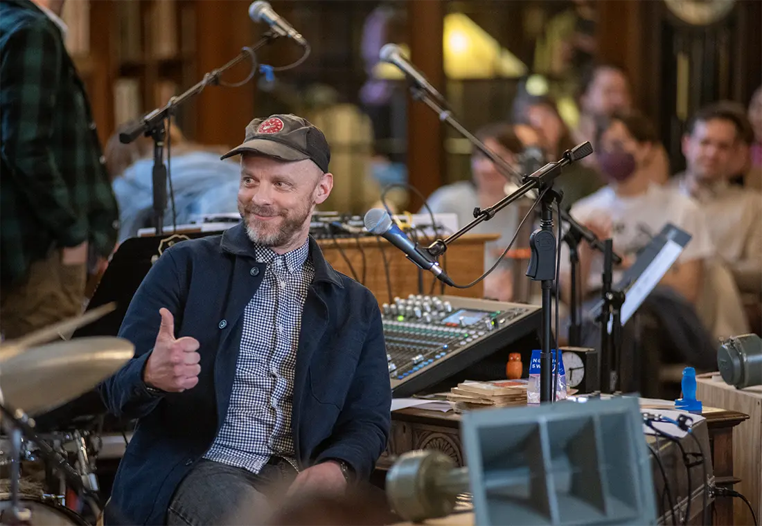 A student sits at a drum set giving a thumbs up to someone behind him.