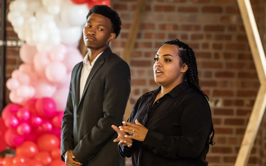 Two students stand at the front of a room speaking.