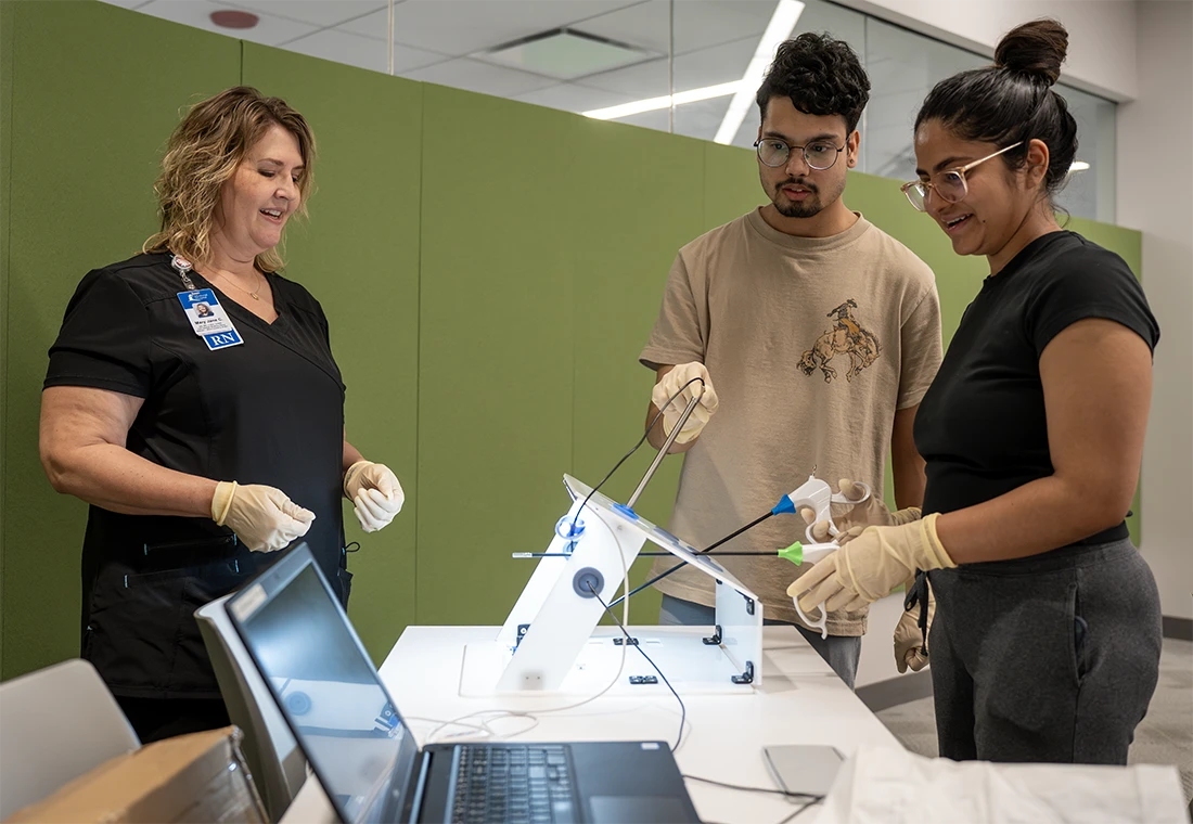 Two students working with a nurse to experiment with equipment.