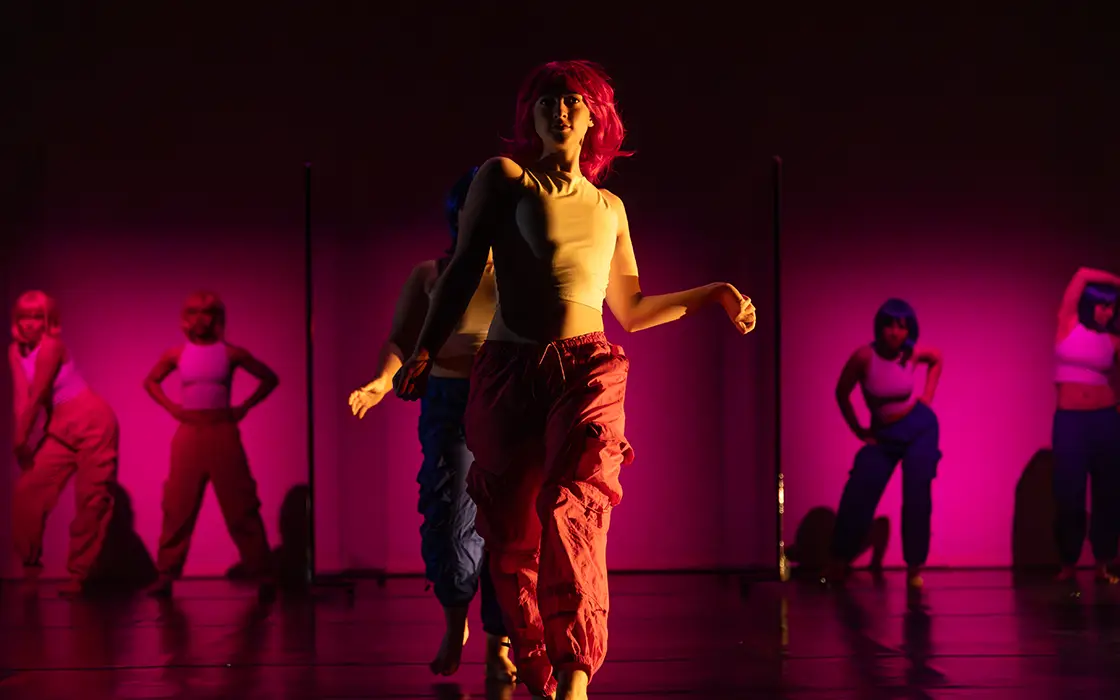 A student dancer is center stage with more students lined up behind her. They are all highlighted in pink. 