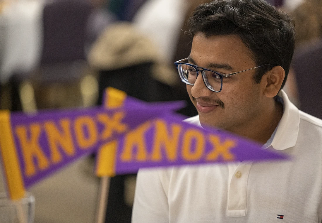 A Knox student sits at a table surrounded by small purple and gold pennants that say Knox.