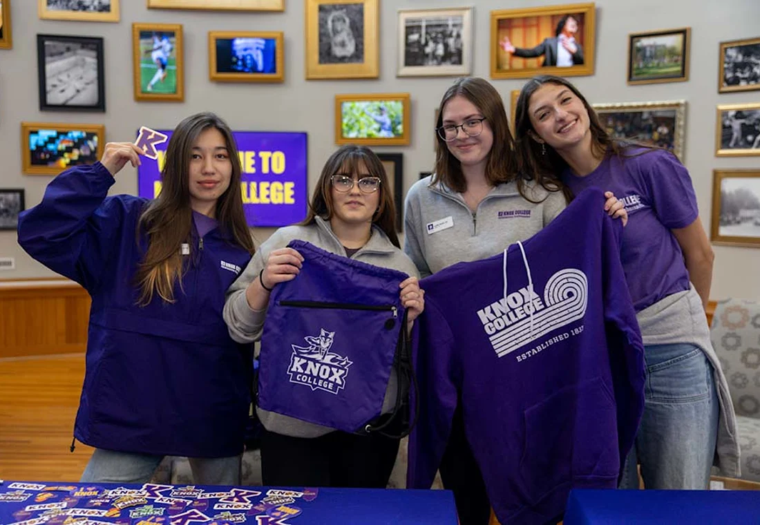 Four individuals smile at the camera, holding up Knox swag. 