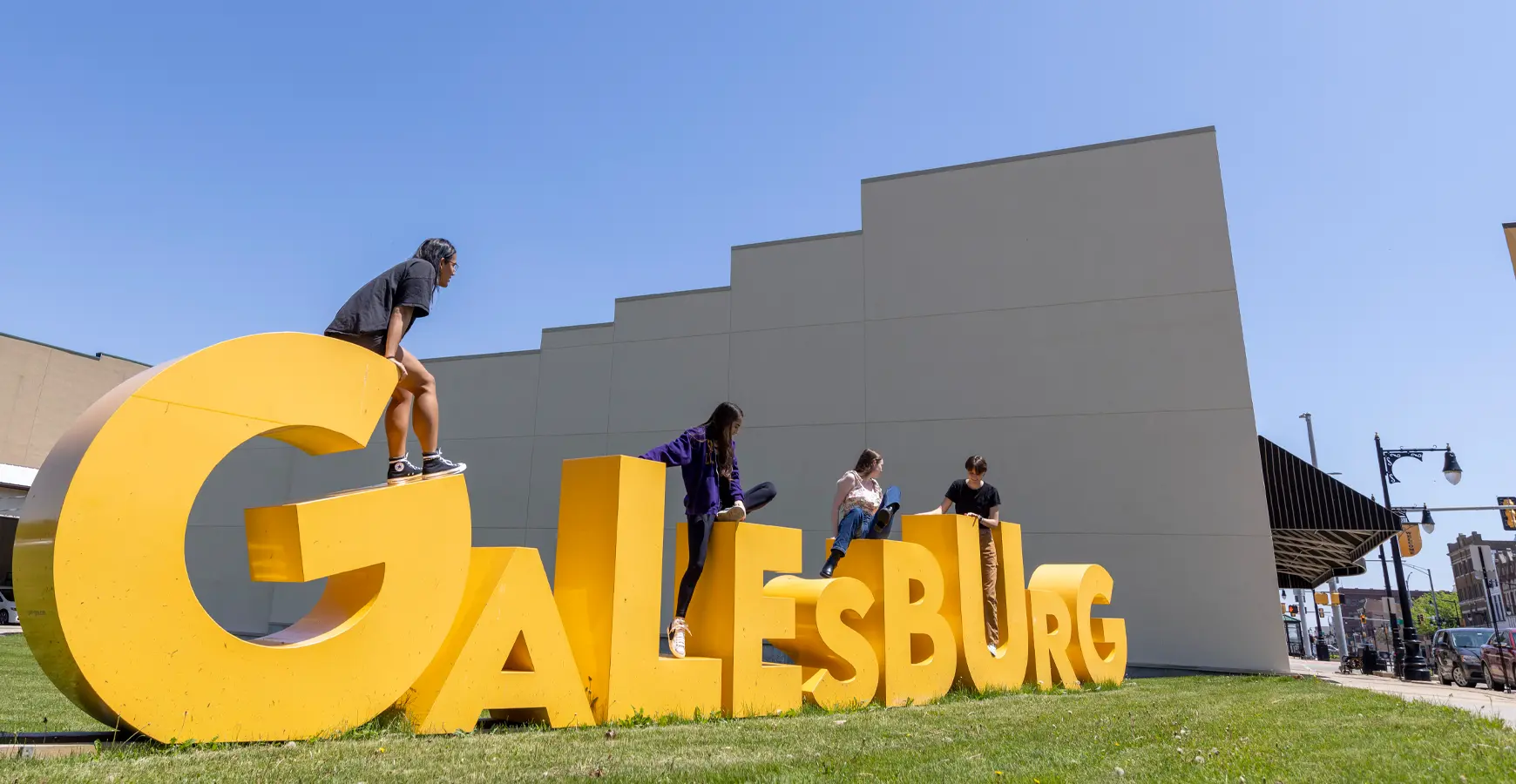 A group of students climbs on a 3d sign that says Galesburg.
