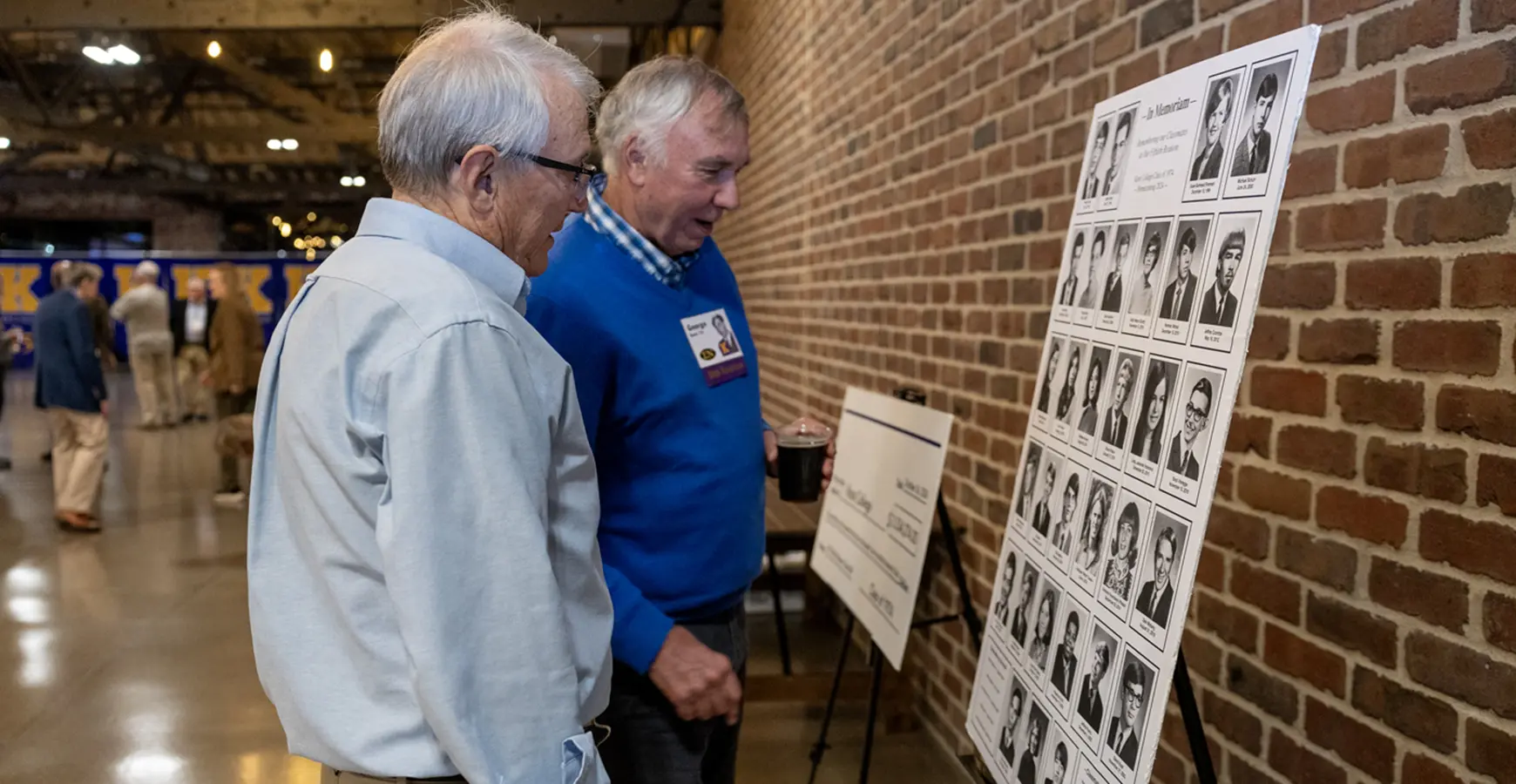 Two members of the Fifty Year Clu look at a series of photos posted on a wall.
