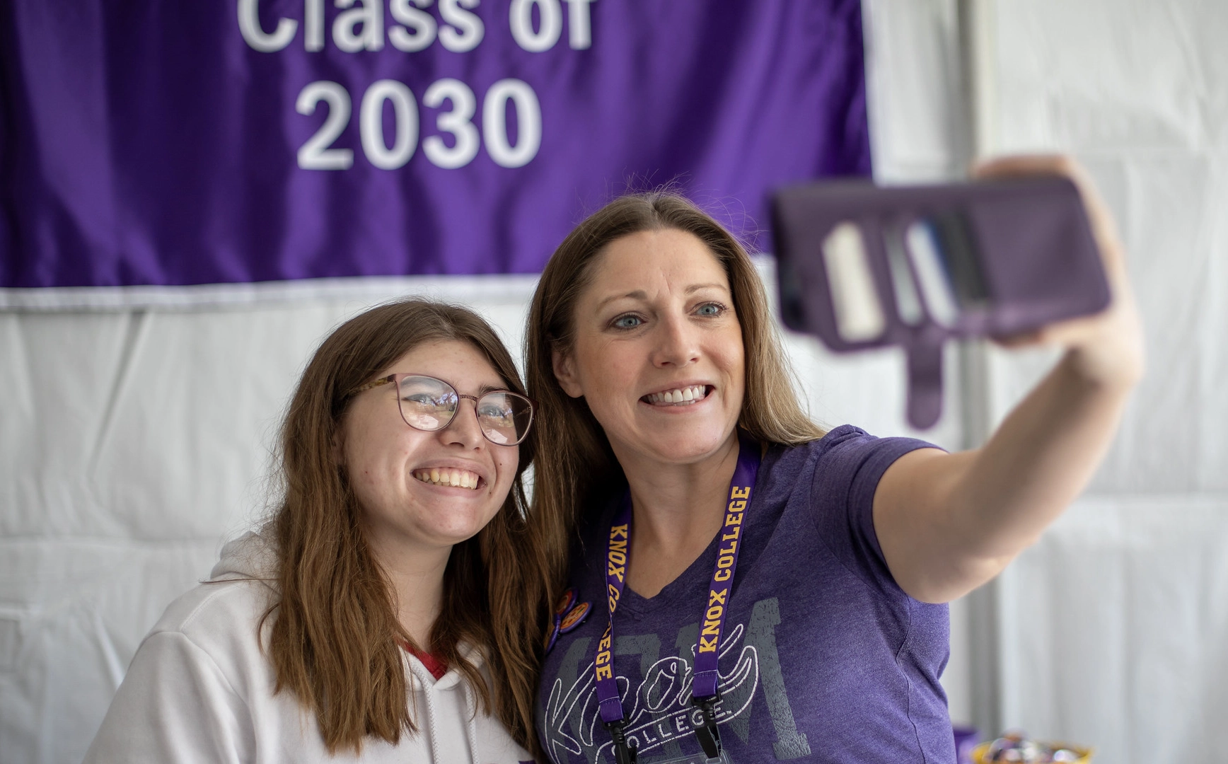 Two women take a selfie in front of a purple Class of 2030 banner.
