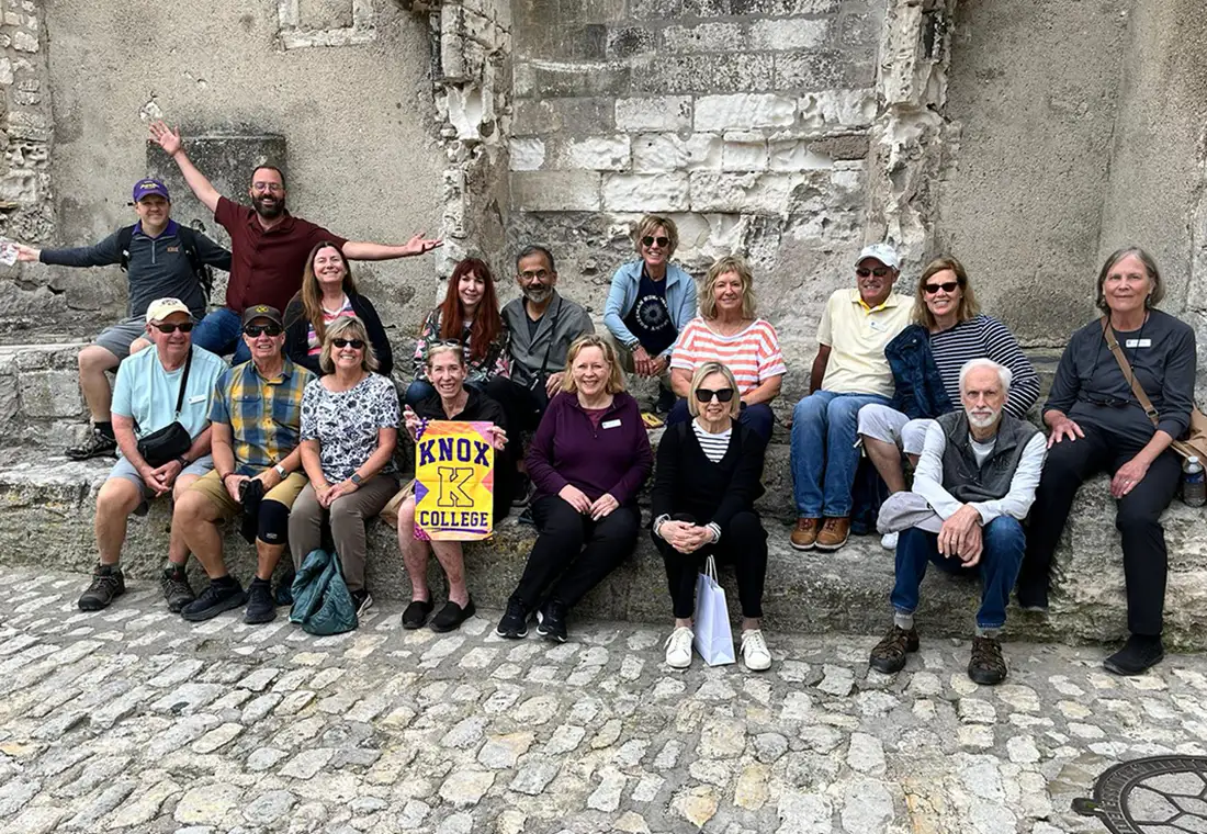 A group of Knox alumni pose on a cobblestone street, holding a Knox banner.