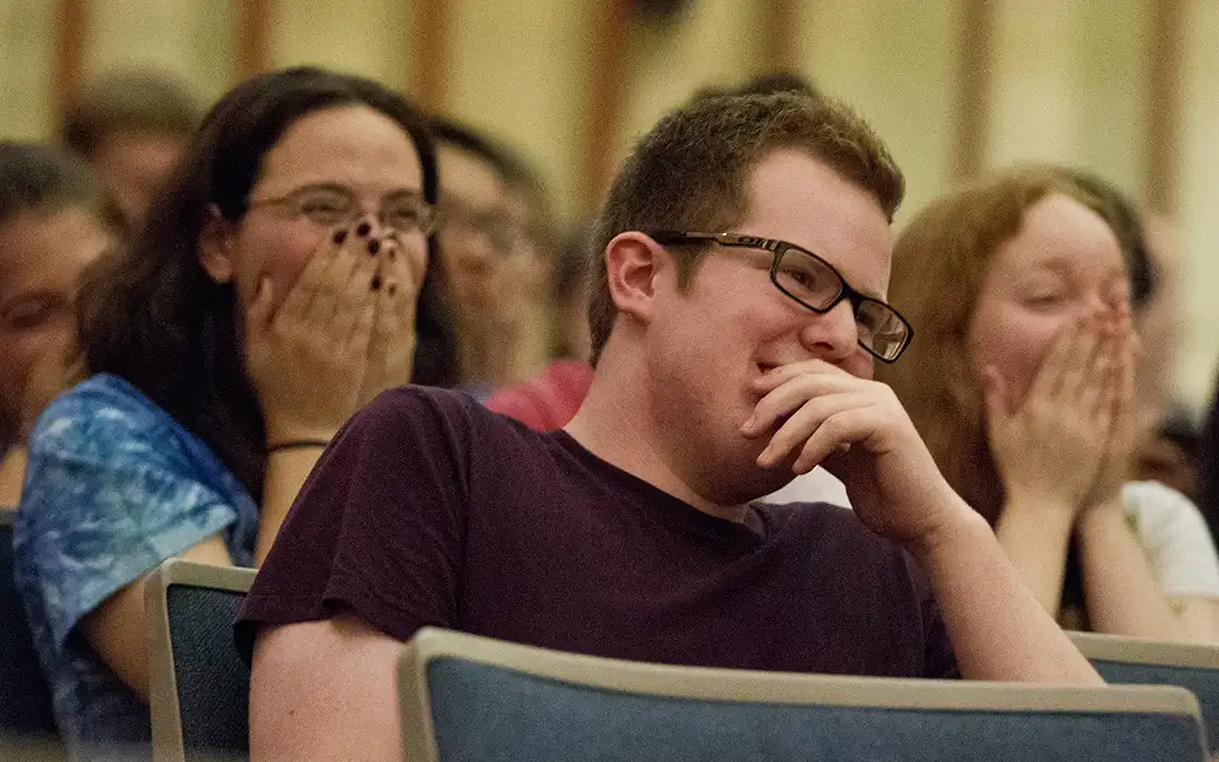 A student sits in a crowd, laughing at the show he is watching.